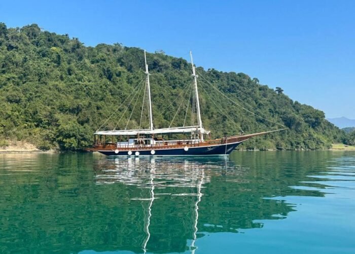 Escuna clássica navegando em águas cristalinas de Paraty, cercada por vegetação tropical.