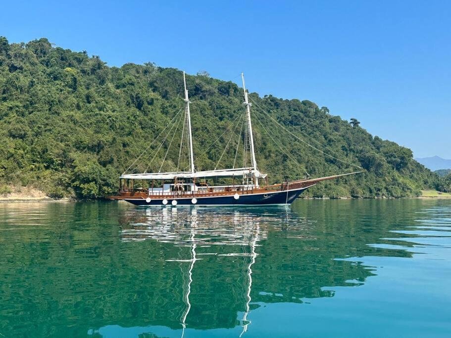 Escuna clássica navegando em águas cristalinas de Paraty, cercada por vegetação tropical.