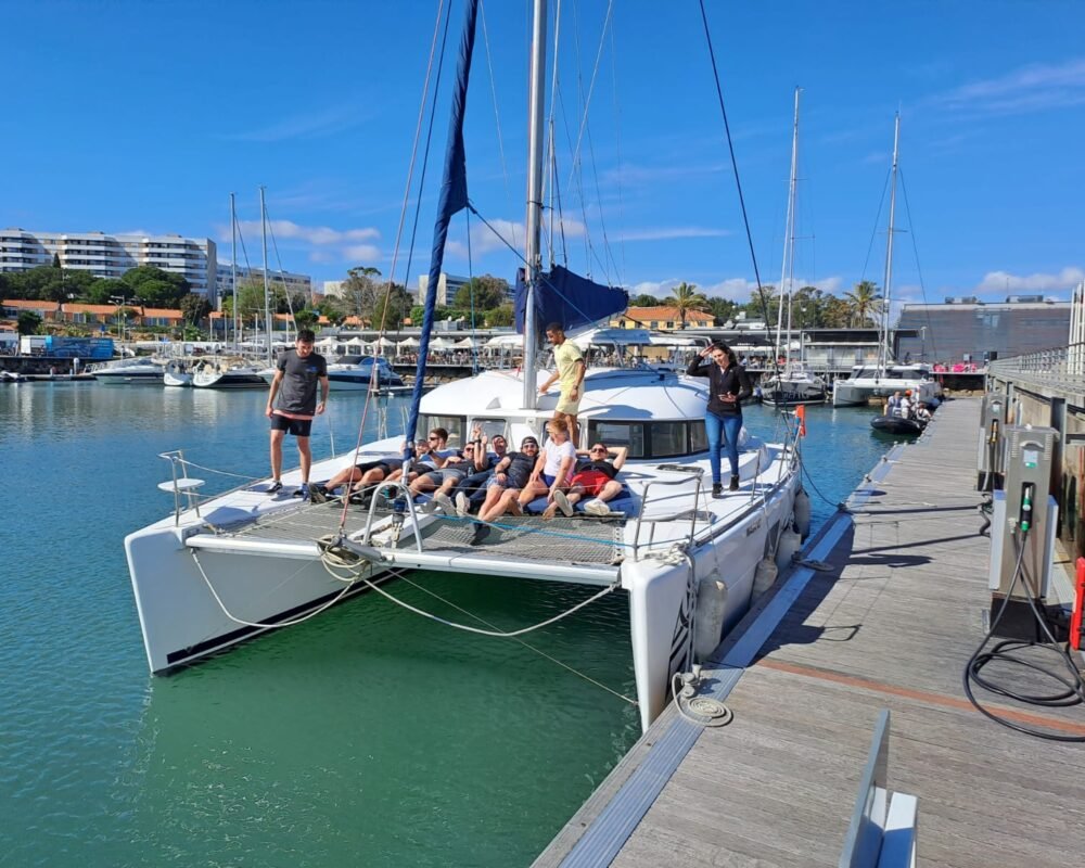 Grupo de amigos relaxando na área da proa do catamarã Lagoon 380 S2, ancorado em Lisboa. Ambiente perfeito para socializar e aproveitar a vista.