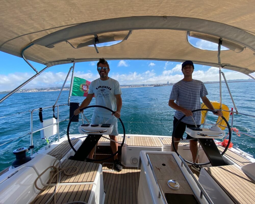 Duas pessoas manobrando o Dufour 360 no mar, com ampla área de cockpit e cobertura de proteção solar.