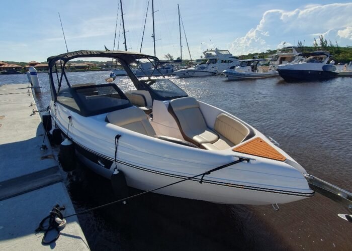 lancha Coral 26 atracada em píer de marina, com bancos bege na proa e veleiros ao fundo