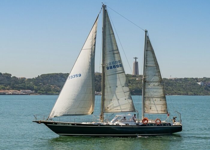 Veleiro com velas abertas navegando, com o Cristo Rei ao fundo.