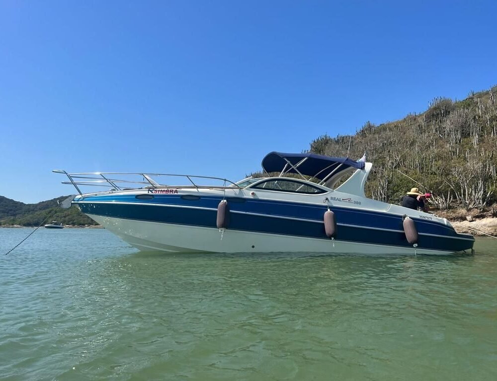 Lancha Real Powerboat 30 pés ancorada em águas claras, com vegetação ao fundo.