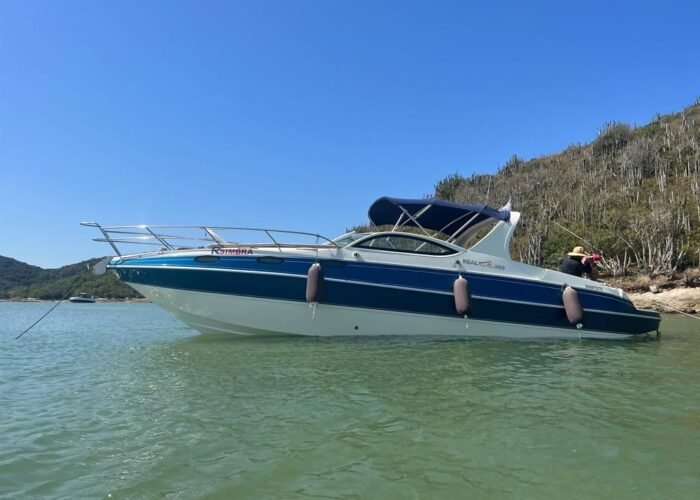 Lancha Real Powerboat 30 pés ancorada em águas claras, com vegetação ao fundo.