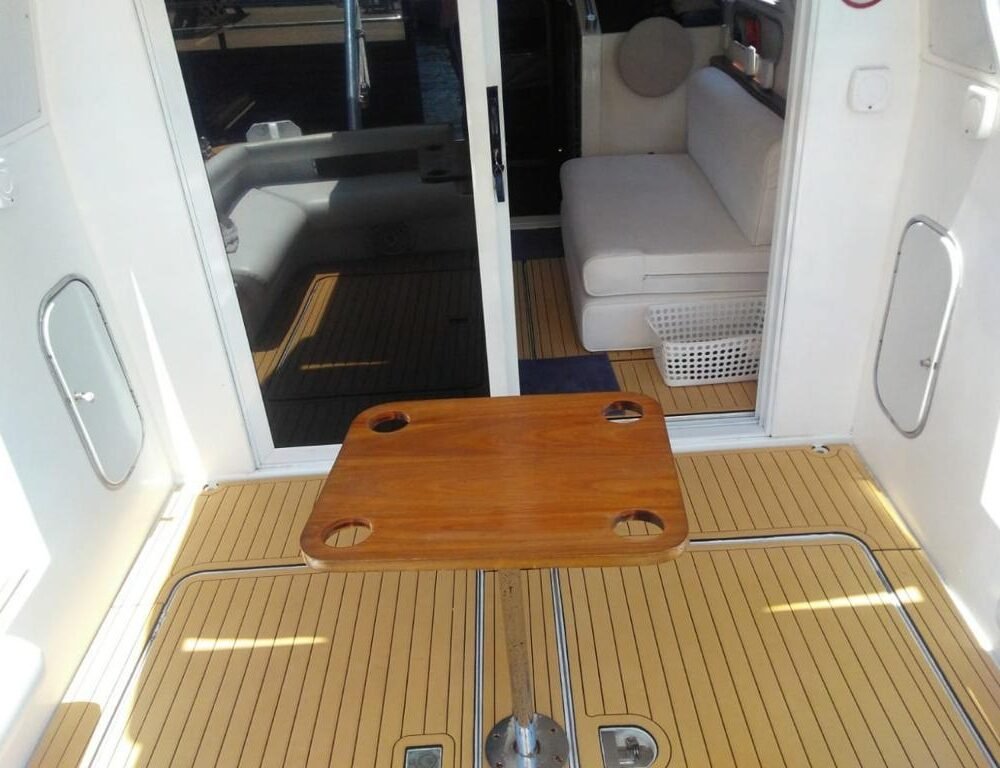 Deck da Lancha Oceanic 32 em Angra dos Reis, mostrando uma entrada para o salão interno e uma mesa de madeira ao centro.