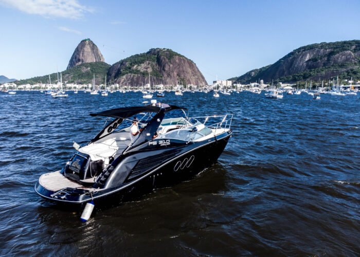 Lancha FS 310 preta e branca no mar com o Pão de Açúcar, o Morro da Urca e veleiros ao fundo