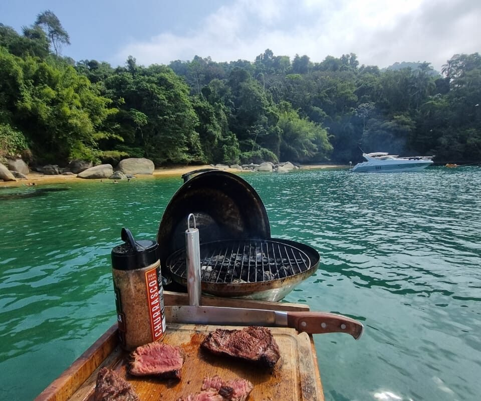 Churrasqueira portátil com carne preparada a bordo da lancha Phantom 29 em uma praia de Angra dos Reis.