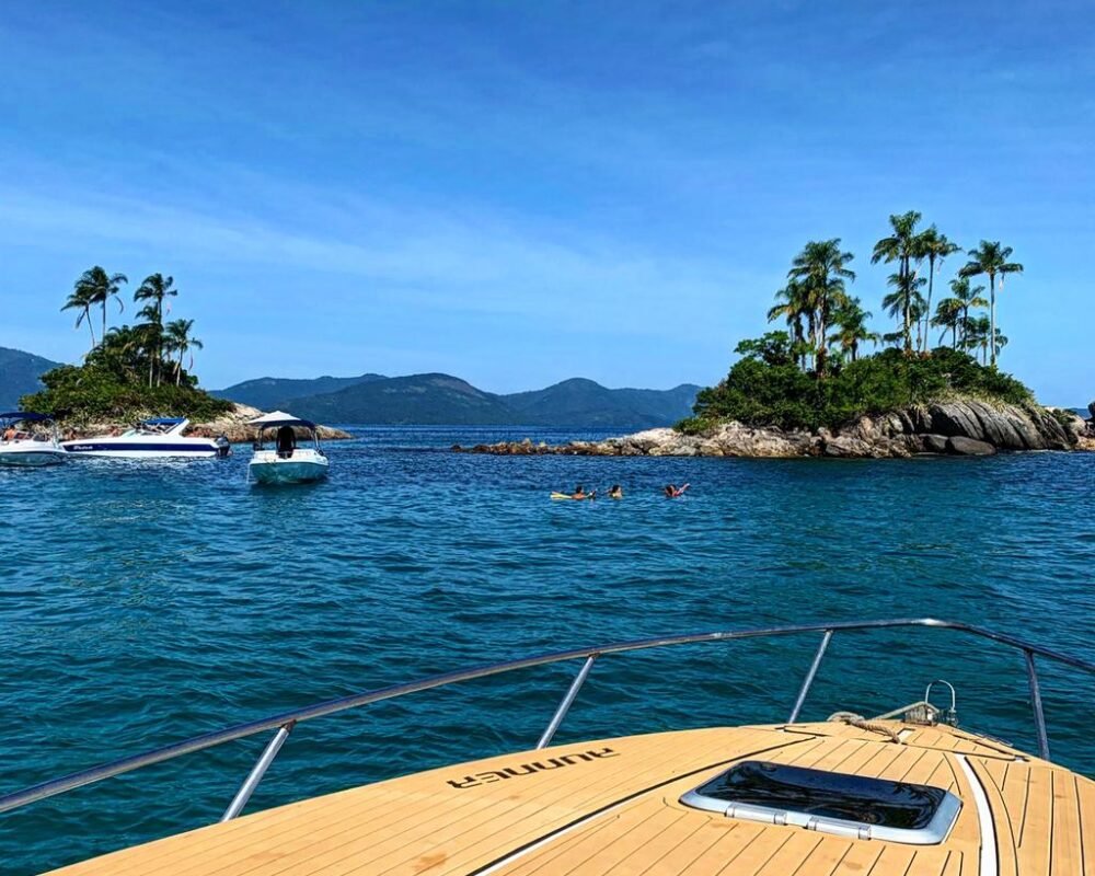 Vista da proa da lancha Runner 29 navegando em águas cristalinas, com ilhas ao fundo em Angra dos Reis.