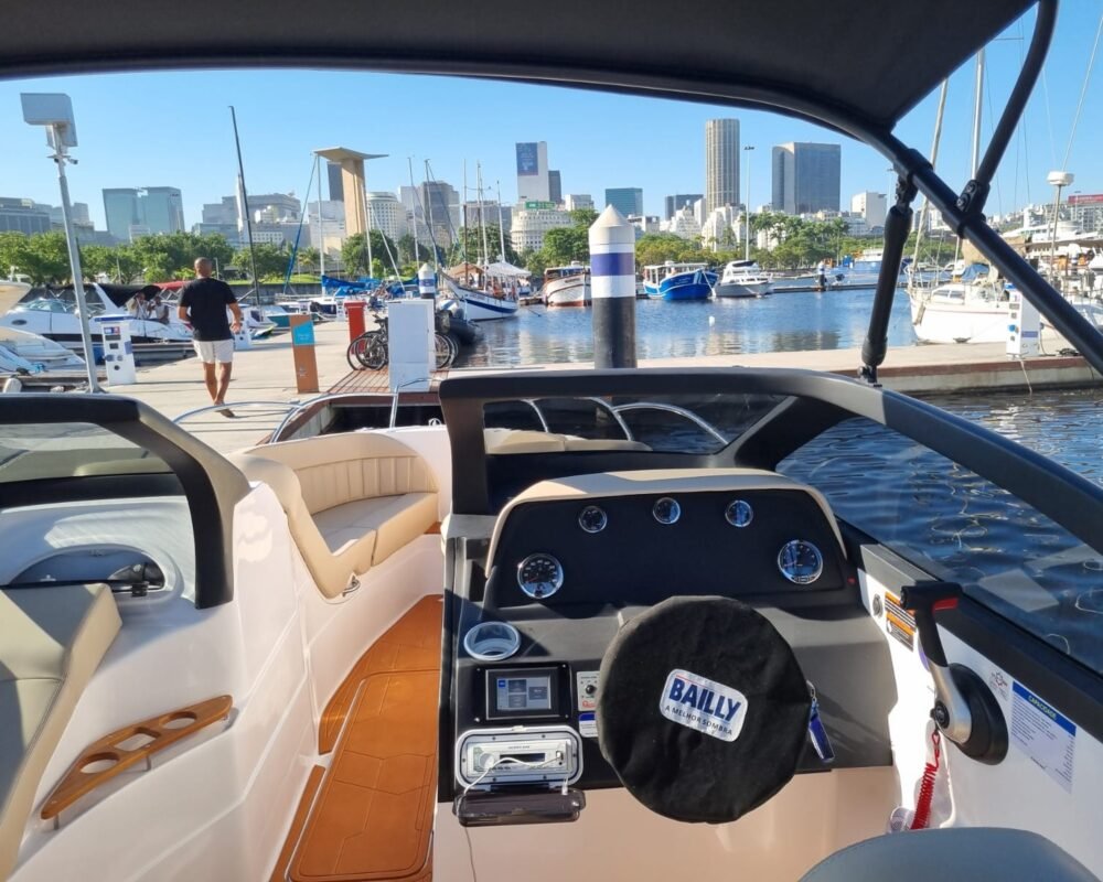 Painel de controle da lancha Coral 26 na Marina da Glória, com vista para os prédios do Rio de Janeiro ao fundo.