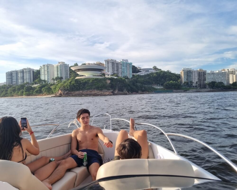 Jovens relaxando a bordo da lancha Coral 26, navegando pela Baía de Guanabara com vista para Niterói.