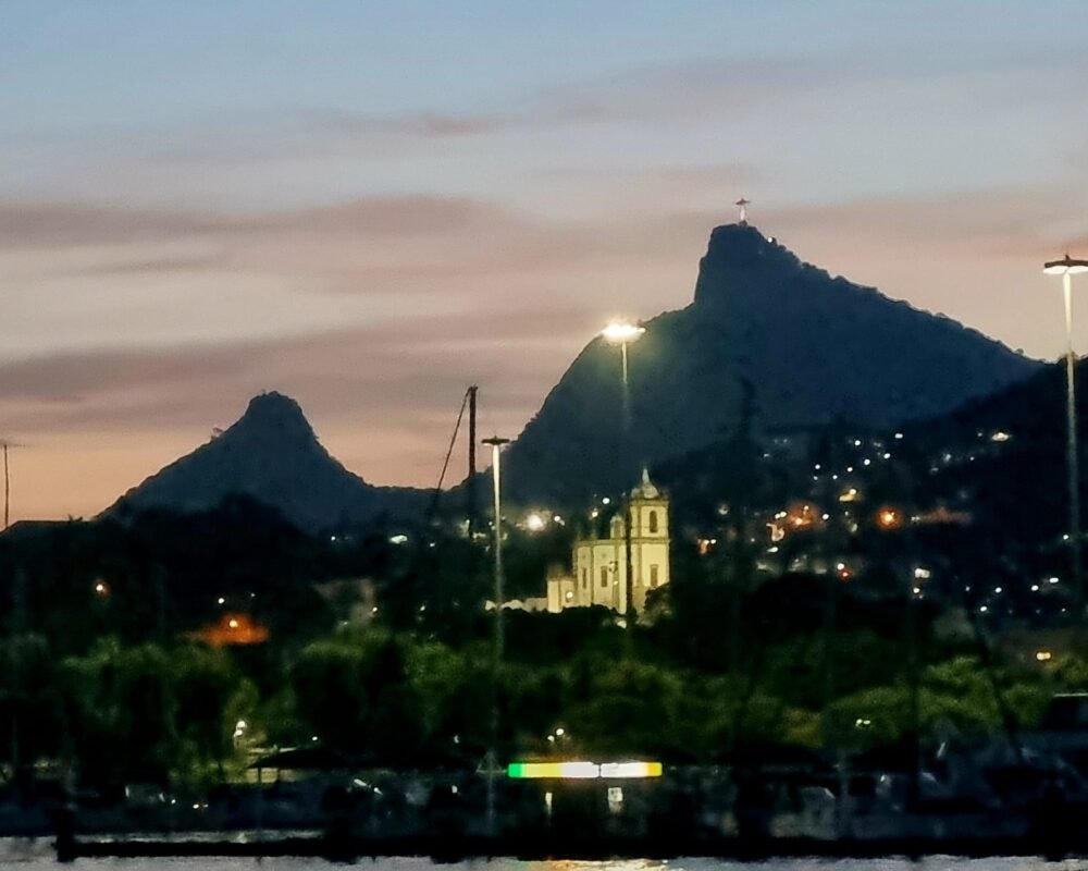 Cristo Redentor iluminado ao entardecer, visto da Baía de Guanabara durante um passeio de lancha.