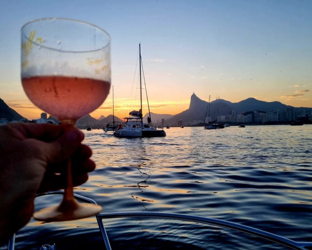 Brinde com taça de vinho rosé a bordo da lancha Coral 26, com o Pão de Açúcar ao fundo.