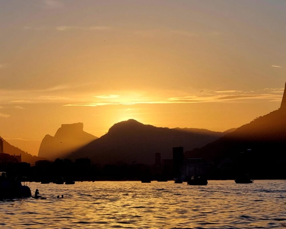 Silhueta do Cristo Redentor e das montanhas do Rio de Janeiro ao pôr do sol, vista do mar.