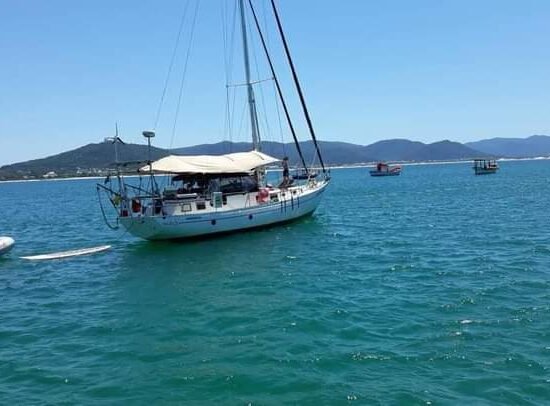 Veleiro Florianópolis ancorado em águas azuis, com botes e pranchas de stand-up paddle disponíveis para diversão.