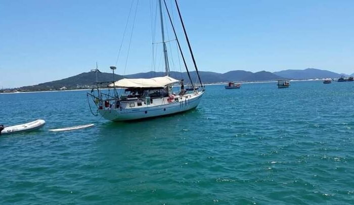 Veleiro Florianópolis ancorado em águas azuis, com botes e pranchas de stand-up paddle disponíveis para diversão.