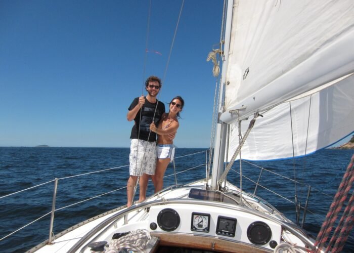 Casal navegando e aproveitando as paisagens naturais a bordo do passeio de veleiro Peterson 33 no Rio de Janeiro.