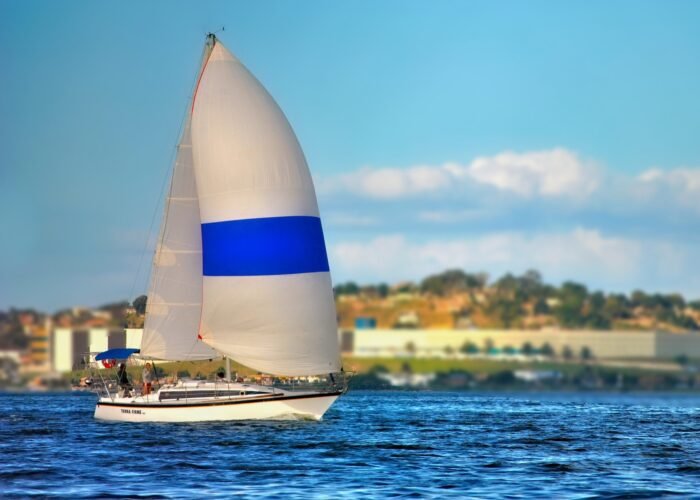 Veleiro Peterson 33 navegando com balão branco e azul aberto em mar azul, com a costa ao fundo