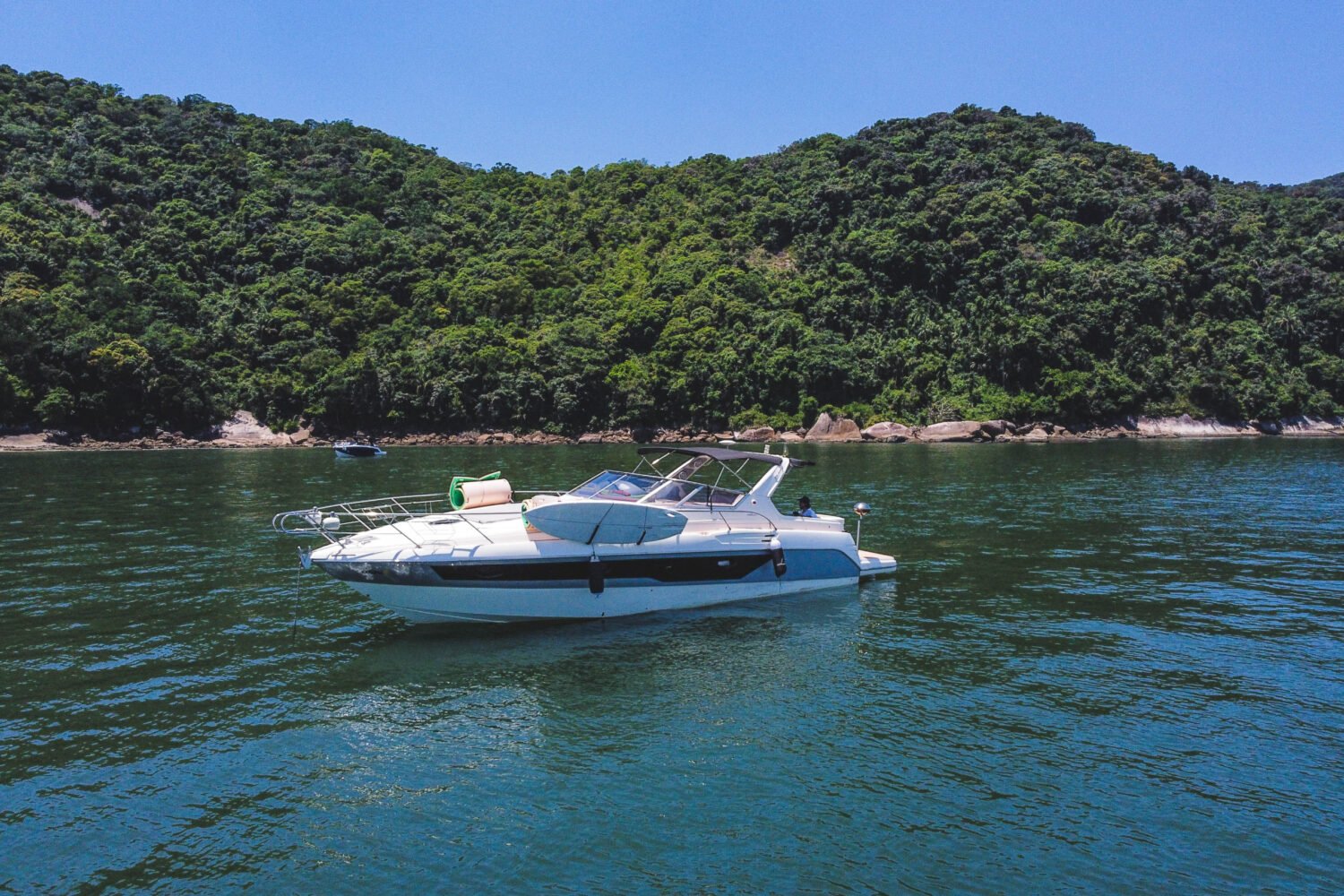 Vista lateral da lancha ancorada em uma praia paradisíaca do Guarujá, ideal para passeios privativos.