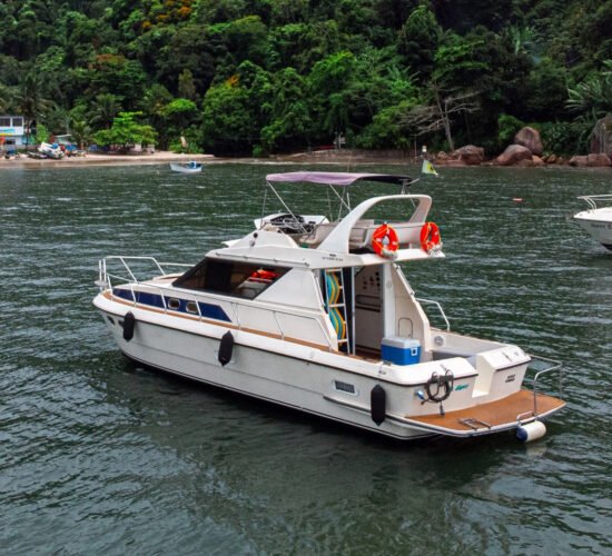 Lancha Oceanic 36 navegando em águas calmas próximas à costa do Guarujá, com vegetação exuberante ao fundo.