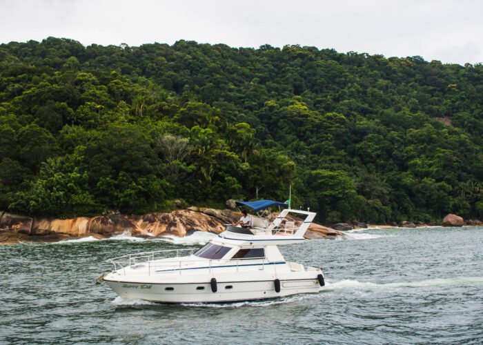 Lancha Sea Baron 38 pés branca navegando próxima a costão rochoso com mata atlântica no Guarujá