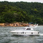 Vista lateral da Lancha Sea Baron 38 em movimento nas águas do Guarujá, cercada por paisagens naturais.