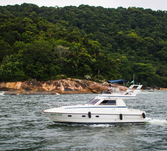 Vista lateral da Lancha Sea Baron 38 em movimento nas águas do Guarujá, cercada por paisagens naturais.