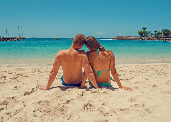 Casal curtindo a praia durante o aluguel de barco para lua de mel, com vista para o mar e veleiros ao fundo.