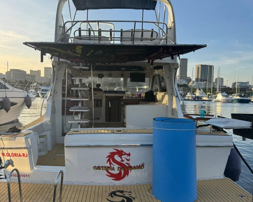 Popa da lancha com nome Caverna do Dragão e logo em vermelho, deck em teca, marina e skyline do Rio ao fundo