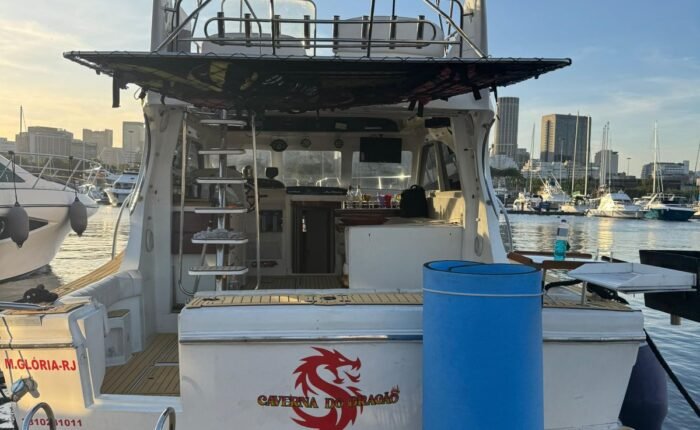Popa da lancha com nome Caverna do Dragão e logo em vermelho, deck em teca, marina e skyline do Rio ao fundo