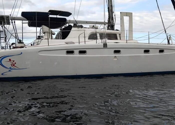 Catamarã Dolphin 46 fundeado, visto de perfil, com mastro, bimini, painéis solares e bandeira do Brasil