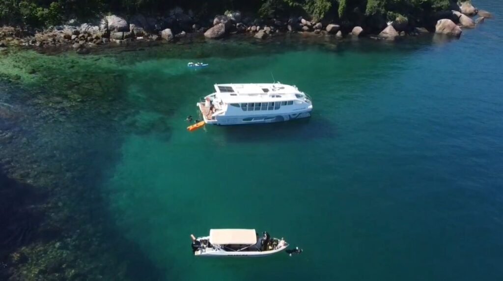 Vista aérea do Catamarã Casamarã em Angra dos Reis com bote de apoio e passageiros nadando.