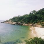 Praia Adão e Eva em Niterói, com água verde-esmeralda, areia branca e vegetação de Mata Atlântica ao fundo