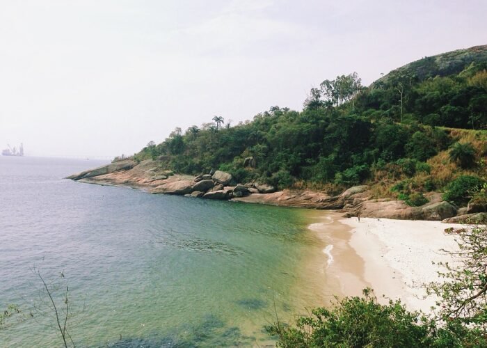 Praia Adão e Eva em Niterói, com água verde-esmeralda, areia branca e vegetação de Mata Atlântica ao fundo