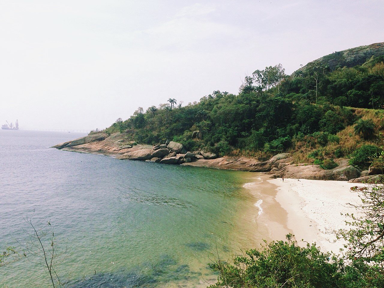 Praia Adão e Eva em Niterói, com água verde-esmeralda, areia branca e vegetação de Mata Atlântica ao fundo