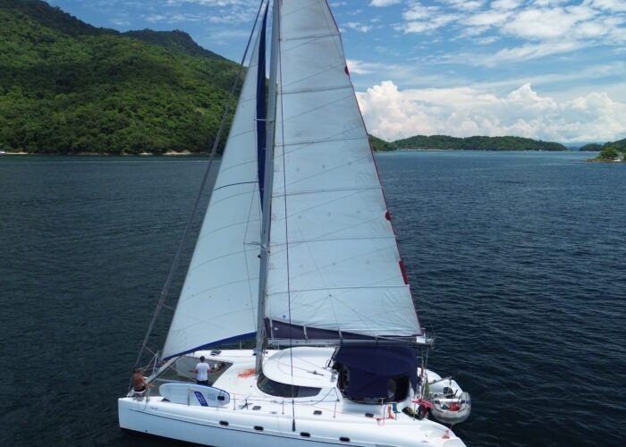 catamarã Fountaine Pajot 46 navegando com velas içadas, perto de morro com mata e ilhas ao fundo