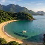 Praia paradisíaca de Ilhabela acessível apenas por barco, com lancha ancorada em águas cristalinas e montanhas cobertas de Mata Atlântica ao fundo