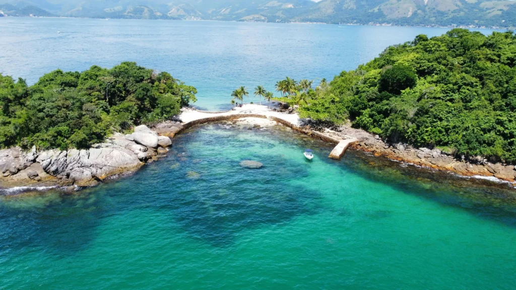 Vista aérea de ilha em Angra dos Reis com águas cristalinas verde-esmeralda, coqueiros e lancha ancorada