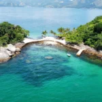 Vista aérea de ilha em Angra dos Reis com águas cristalinas verde-esmeralda, coqueiros e lancha ancorada