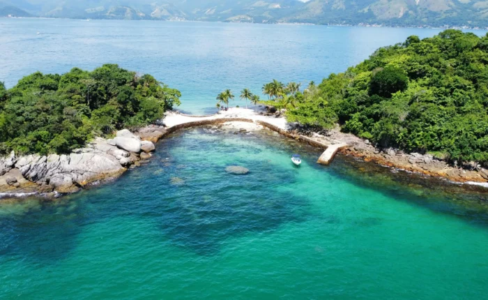 Vista aérea de ilha em Angra dos Reis com águas cristalinas verde-esmeralda, coqueiros e lancha ancorada
