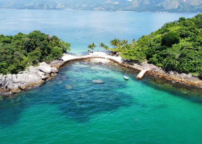 Vista aérea de ilha em Angra dos Reis com águas cristalinas verde-esmeralda, coqueiros e lancha ancorada