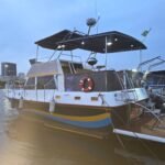 Trawler Sereno III atracado em marina ao entardecer, com flybridge coberto e skyline do Rio de Janeiro ao fundo.