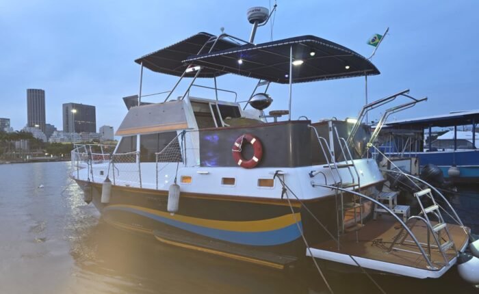 Trawler Sereno III atracado em marina ao entardecer, com flybridge coberto e skyline do Rio de Janeiro ao fundo.
