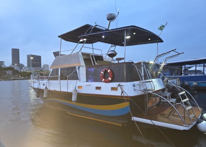Trawler Sereno III atracado em marina ao entardecer, com flybridge coberto e skyline do Rio de Janeiro ao fundo.