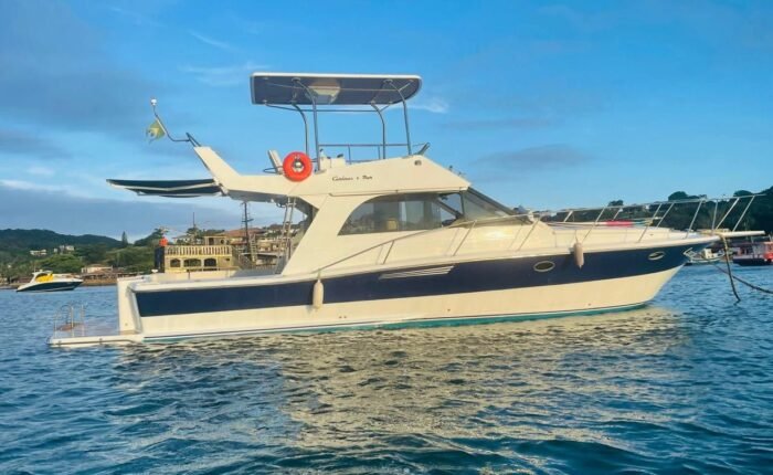 Lancha Carbrasmar ancorada em enseada, com casco azul e branco e flybridge coberto