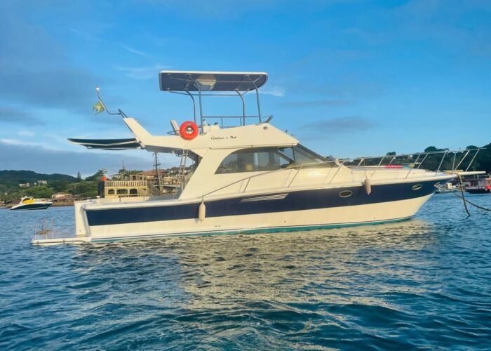 Lancha Carbrasmar ancorada em enseada, com casco azul e branco e flybridge coberto