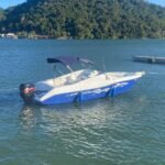 Lancha Alternativa 22 ancorada em Angra dos Reis, com casco azul e branco e morro coberto de mata ao fundo