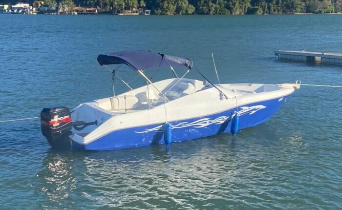 Lancha Alternativa 22 ancorada em Angra dos Reis, com casco azul e branco e morro coberto de mata ao fundo