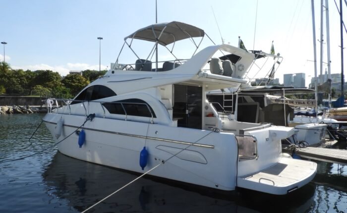 Perfil da lancha branca de 36 pés atracada, com salão fechado, flybridge e defensas azuis
