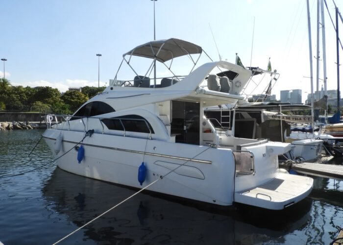 Perfil da lancha branca de 36 pés atracada, com salão fechado, flybridge e defensas azuis