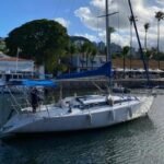 Veleiro Fast 395 atracado em marina, com mastro alto, capa azul da vela e palmeiras ao fundo